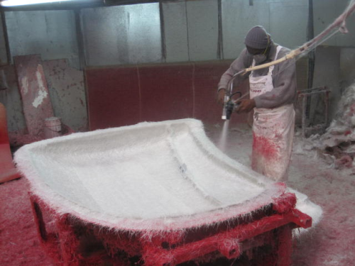 Figure 1: Typical open mould operation using chopper spray of resin and glass fibre before worker hand consolidation.