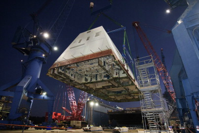 The 1,000-ton deckhouse of destroyer USS Zumwalt (DDG 1000) is craned toward the deck of the ship at General Dynamics Bath Iron Works. The deckhouse is primarily made from balsa-cored carbon fiber using VARTM. Photo used with permission © U.S. Navy.