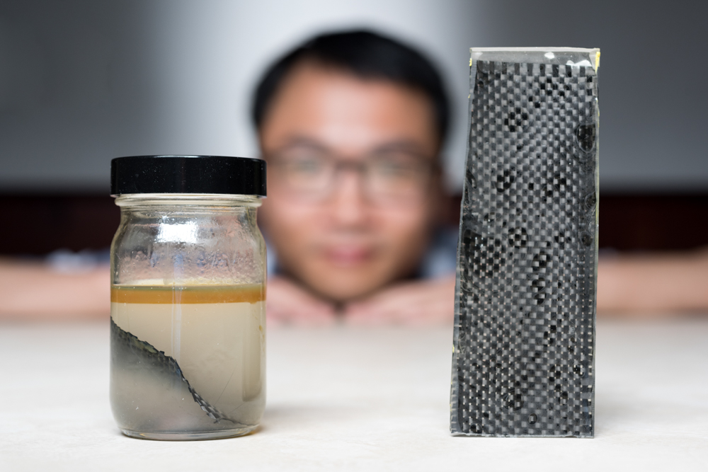 Kai Yu, a former postdoctoral researcher in The George W. Woodruff School of Mechanical Engineering at Georgia Tec, sits behind a piece of carbon fiber composite immersed in alcohol. (Credit: Rob Felt, Georgia Tech).