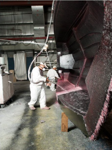Regal Boats operators spraying Owens Corning's OptiSpray rovings onto a complex mould. Regal has found that OptiSpray reduces the amount of resin it uses, leading to savings in both money and boat weight.